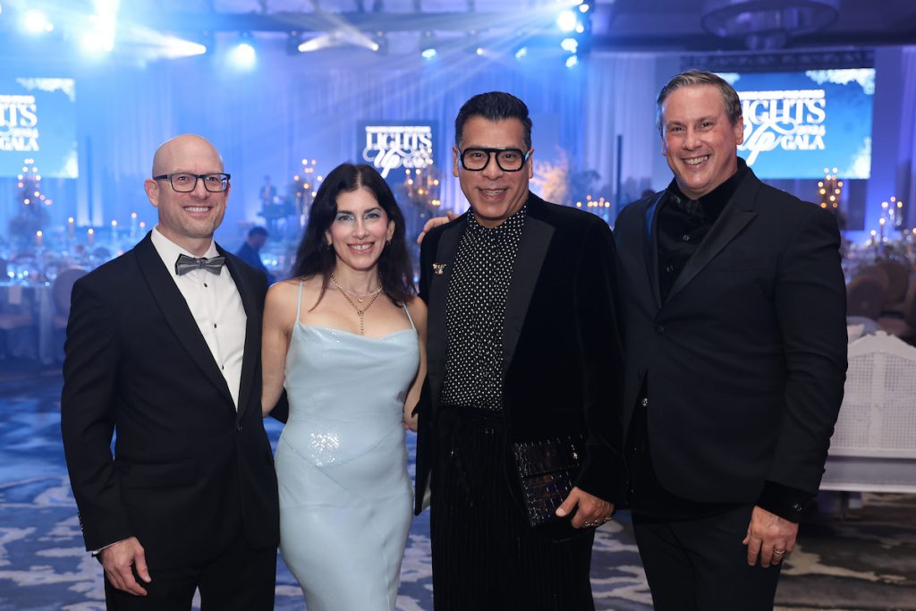 Four guests in formal attire smile at the camera at a gala event.